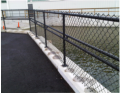 Powder coated chain link fence base plated to concrete blocks, with a grab rail 
